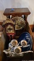 Box showing two tabletop clocks, silver-tone reindeer candelabra, Danish plate, and Delft container