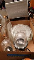Box containing multiple glass serving plates and Magic Bullet blender components showing normal wear