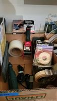 Overview photo of various electric tools and tape dispensers in a cardboard box.