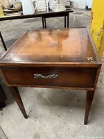 Front view of vintage side table showing square top with inlaid leather-like panel with decorative gold fleck border and tapered legs.