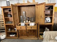 Front view of the solid oak entertainment center showing the central cabinet with doors open revealing interior shelves and two drawers below, flanked by open shelving on end units containing various decorative items.