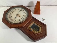 Clinton wall clock face, pendulum compartment visible, Seth Thomas metronome and winding key beside clock on surface