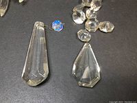 Close-up photo showing two large clear crystal pendants with faceted cuts and an iridescent octagonal crystal connector with a small hook on a black background.