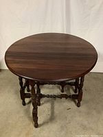 Front view of the round drop leaf table with all leaves raised, showing turned legs and wooden top.