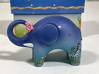 Side view of blue elephant bisque figurine showing artwork and details with pink flower on trunk