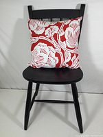 Black painted Heywood Wakefield wooden chair with red and white floral pillow placed on the seat against a white backdrop.