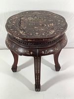 Front view of a Japanese wooden stool showing dark wood, scalloped edges, carved legs, and intricate inlay design on top.