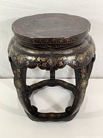 Front view of a round black lacquered wood stool with gold floral decorations and signs of water damage on the top surface.