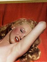 Close-up of Marilyn Monroe’s head and shoulders reclining nude on red background