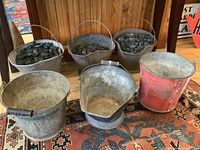 Front view showing three metal coal buckets filled with coal on the top row and three metal pails on the bottom, all placed on a patterned rug.