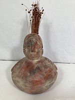 Close-up of rounded pottery vase with face holding dried flowers