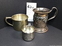 Group shot of all three silver mugs—monogrammed “Jeremy” mug, monogrammed “M” mug, and grape vine motif mug