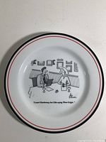 Close-up of one cheese plate showing cartoon illustration and caption: 'I want Chardonnay, but I like saying Pinot Grigio.' Plate round with white background and red and black rim lines.