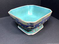 Angled view of square bowl showing turquoise interior, scalloped rim and footed base; exterior cobalt blue floral scroll design