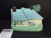 Front angle view of the painted cast iron house doorstop showing blue roof, white walls, and brown chimneys with green foliage base.