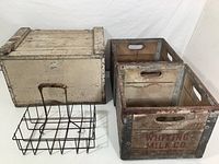 Photo showing two wooden Whiting milk crates, one painted wooden Hood milk box, and a metal rack with four compartments