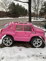 Side view of pink Cadillac styled kids battery car on snow-covered ground, showing detailed body, wheels, windows, and seating area.