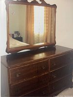 Front view of dresser showing six drawers and attached mirror reflecting window and curtain.