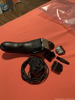 Black Wahl hair cutting machine with blade and some attachments plus charging cord on an orange surface.