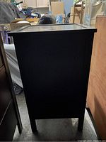 Side view of the small black cabinet showing the solid black painted finish and tapered legs.