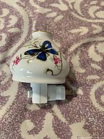 Top and side view of porcelain plug-in night light showing butterfly and floral design on front.