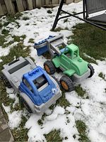 Photo showing two large kids toy trucks placed on snow-covered grass next to a patio swing chair.