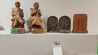 Front view of two carved wooden figures, two solid bronze bookends, and one wooden bookend displayed on a shelf.