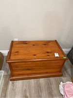 Full frontal image of the wooden chest placed on a floor showing the entire item with side handles and flat top surface.