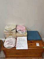 Full lot overview with stacked boxes of collectable plates, some wrapped in paper and a handwritten inventory list on the wooden chest.