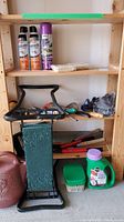 Photo showing insect spray cans, suet bars, various garden tools on wooden shelving, green containers on the floor, and a decorative pink bird clock.