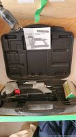 Top-down photo showing closed black plastic carrying case open with Porter-Cable narrow crown stapler inside and instruction manual placed on the lid of the case.