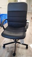 Front view of black office chair showing padded segmented backrest and cushioned seat, with armrests and wheels visible.