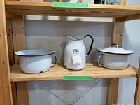 Three white enameled water pots/pitcher on wooden shelf showing wear and chips