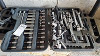 Open black plastic carrying case with various sockets, ratchets, extensions, screwdriver handle adaptor and wrench inside, showing the full contents.