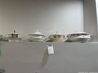 Front view of four porcelain serving pots arranged in a row on a shelf, showcasing various floral designs and lid handles.