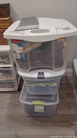 Stack of three plastic storage bins containing sewing notions including fabric, patterns, and other materials labeled as 'Season Clothes - Unfinished'