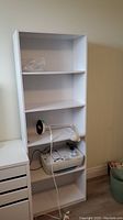 Front view of the white adjustable shelf unit showing four shelves, two with items placed on them.