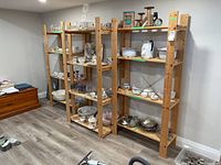 Three wooden shelving units placed side by side in a basement room. Shelves filled with various dishes and odds and ends, demonstrating shelf use and size.