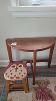Wood demi-lune side table and children's owl-design stool visible together in the room against wall