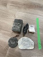 Set of four soapstone carvings displayed on wooden floor, includes two rectangular engraved blocks, one bird figurine, and one round carved medallion with leather string.