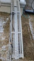 Full length view of the steel ramp showing diamond mesh surface, straps attached for securing.