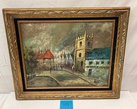 Full view of the framed oil painting depicting a European street scene showing buildings and people.