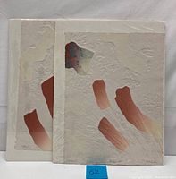 Two abstract pressed paper art prints stacked, showing textured cream paper with abstract reddish and green shapes.