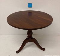 Full view of round wooden side table with carved pedestal and three legs.