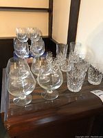 Full lot showing all different types of glasses on wooden table with natural light from window