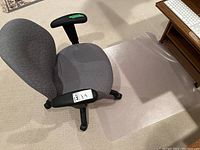 Gray upholstered office chair with adjustable armrests and rolling wheels placed on carpet, with a clear plastic mat beside it