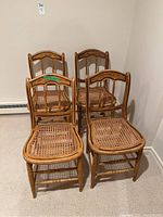 Four wooden chairs with cane seats arranged in a cluster, showing front view and seat condition.