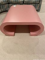 Front view of pink coffee table showing scroll-shaped sides and overall condition