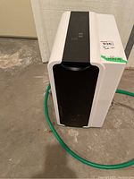 Front and side view of the Classic dehumidifier placed on a concrete floor with a green hose attached.
