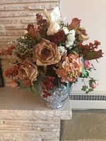 Wide shot of faux flower arrangement in clear glass vase with glass beads, showing variety of flowers and natural looking colors.